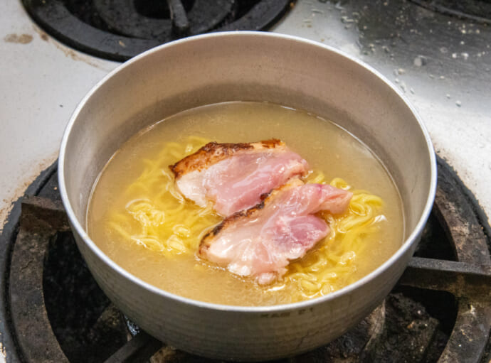 信玄鶏のもも肉と冷凍麺を鶏ガラスープで煮ている様子